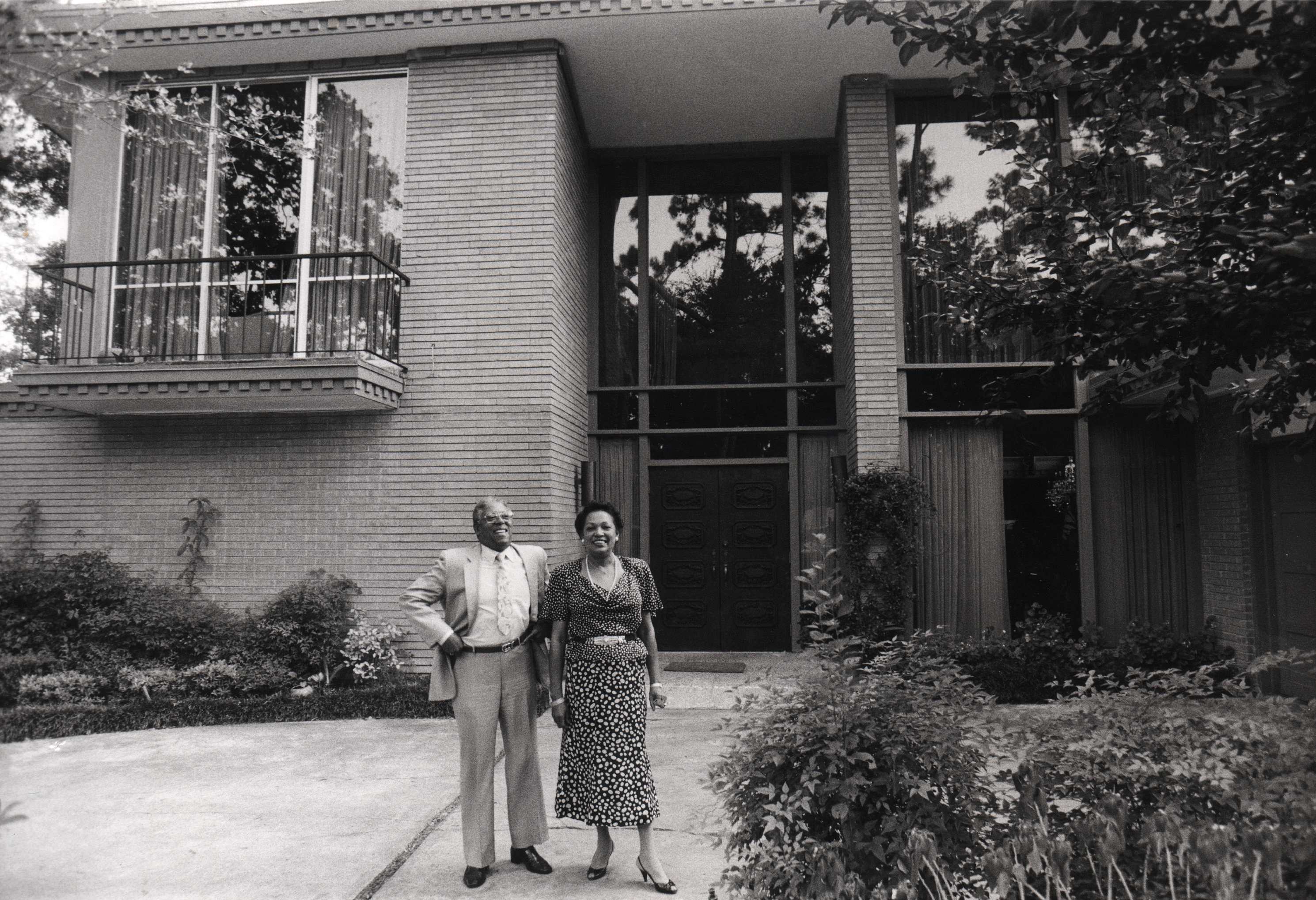 A black couple stands in front of a large modern style house.